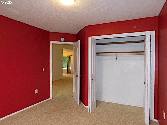 unfurnished bedroom with a textured ceiling, light carpet, and a closet