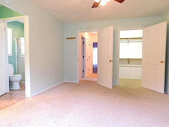 unfurnished bedroom featuring light carpet, a walk in closet, ensuite bath, ceiling fan, and a closet