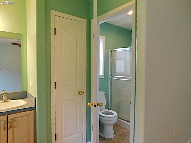 bathroom featuring a shower with door, vanity, and toilet