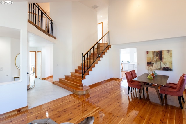 dining space with hardwood / wood-style flooring, stairs, a high ceiling, and baseboards