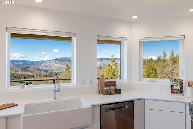 kitchen featuring a mountain view, stainless steel dishwasher, a sink, light countertops, and white cabinets