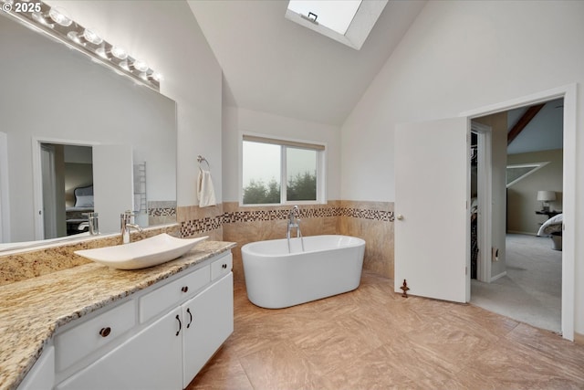 bathroom featuring high vaulted ceiling, a skylight, tile walls, vanity, and a washtub