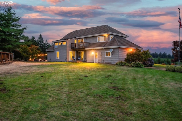 back house at dusk with a balcony and a lawn