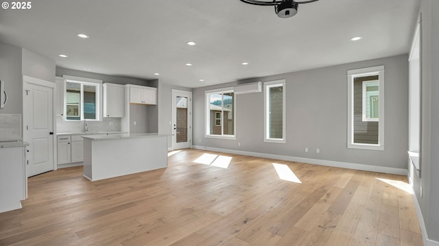 kitchen featuring a wall mounted air conditioner, tasteful backsplash, a kitchen island, light hardwood / wood-style flooring, and white cabinetry