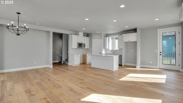 kitchen featuring backsplash, an inviting chandelier, light wood-type flooring, a kitchen island, and white cabinetry