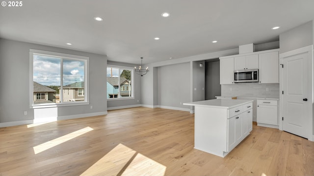 kitchen with pendant lighting, a center island, an inviting chandelier, white cabinets, and light hardwood / wood-style flooring