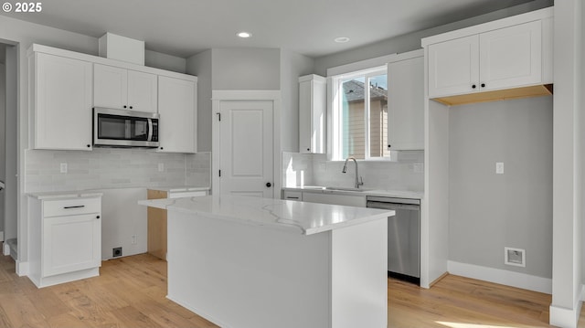 kitchen featuring white cabinets, stainless steel appliances, a kitchen island, and tasteful backsplash