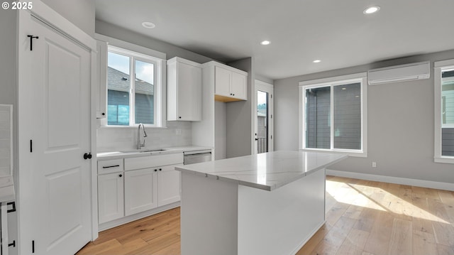 kitchen with a wall mounted air conditioner, light stone countertops, sink, a center island, and white cabinetry