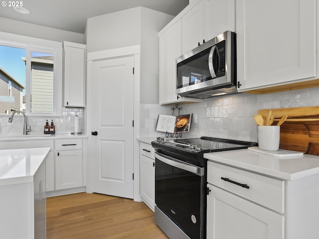 kitchen featuring backsplash, white cabinets, sink, light wood-type flooring, and appliances with stainless steel finishes