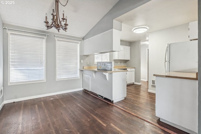 kitchen featuring a breakfast bar, white cabinetry, white refrigerator, dark hardwood / wood-style floors, and kitchen peninsula