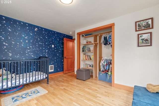 bedroom with visible vents, wallpapered walls, baseboards, wood finished floors, and a closet