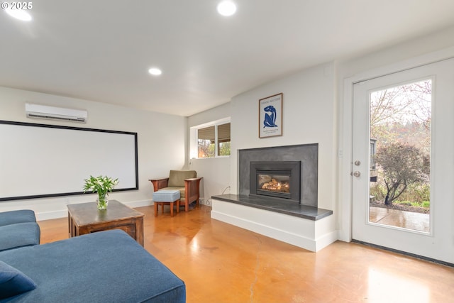 home theater room featuring an AC wall unit, a glass covered fireplace, recessed lighting, baseboards, and concrete flooring