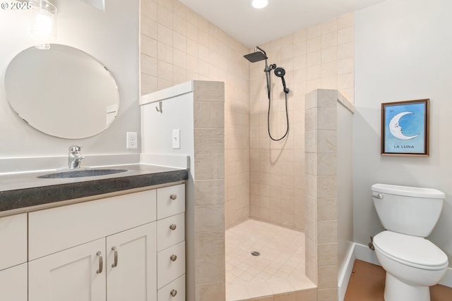 bathroom with a tile shower, toilet, vanity, and baseboards