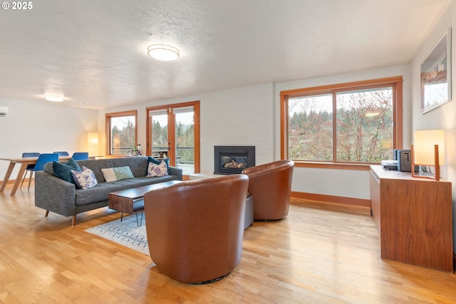 living area featuring light wood-style flooring, a textured ceiling, a large fireplace, and baseboards