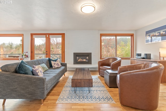 living room featuring light wood-style floors, a healthy amount of sunlight, a fireplace, and a textured ceiling