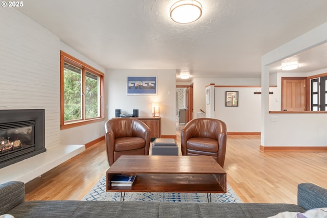 living room with a fireplace, a textured ceiling, baseboards, and wood finished floors