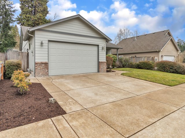 view of front facade featuring driveway, a garage, brick siding, fence, and a front yard