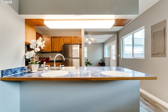 kitchen featuring sink, kitchen peninsula, stainless steel refrigerator, ceiling fan, and electric panel