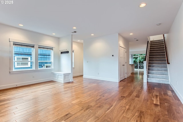 unfurnished living room with light wood-style flooring, stairway, baseboards, and recessed lighting