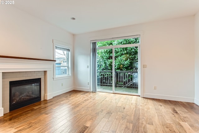 unfurnished living room featuring a brick fireplace, wood finished floors, and baseboards