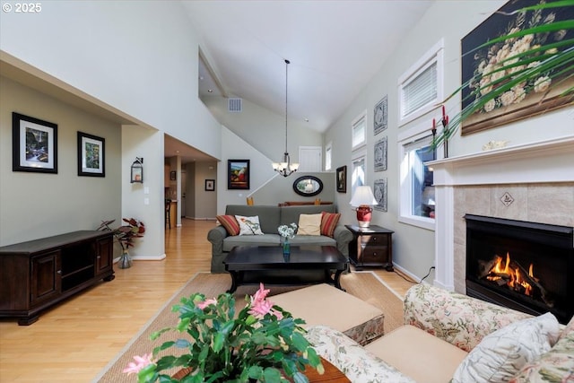 living area featuring visible vents, an inviting chandelier, high vaulted ceiling, a tiled fireplace, and light wood finished floors