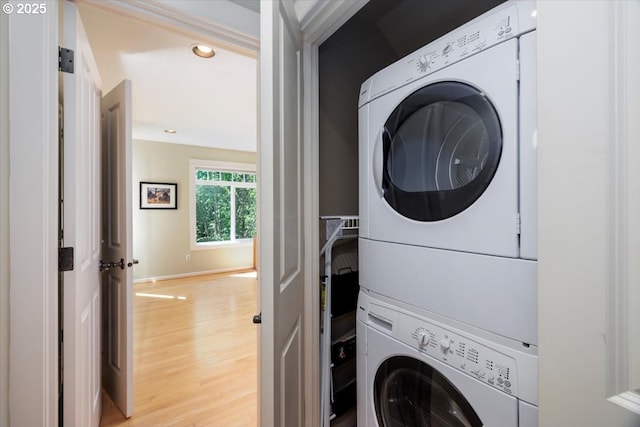 laundry area featuring laundry area, stacked washer and clothes dryer, baseboards, light wood-type flooring, and recessed lighting