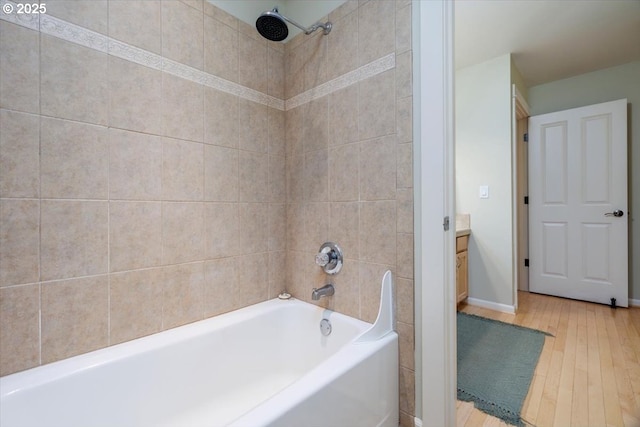 full bath with wood-type flooring, washtub / shower combination, baseboards, and vanity