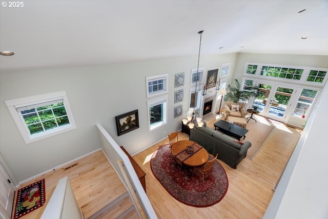 living room featuring visible vents, french doors, wood finished floors, vaulted ceiling, and a lit fireplace