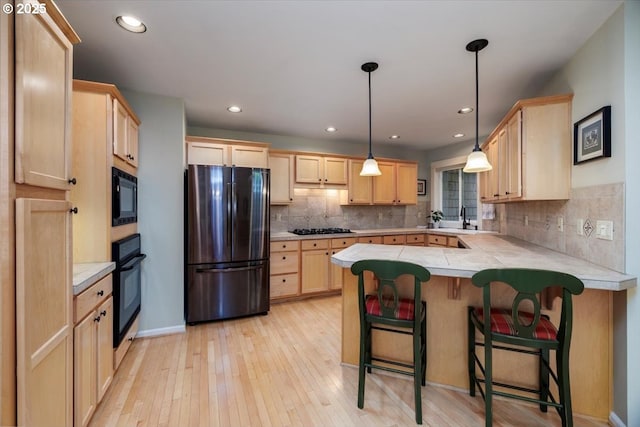 kitchen featuring light brown cabinetry, light countertops, light wood-style flooring, a peninsula, and black appliances