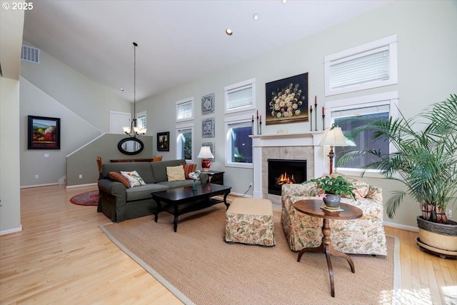 living area featuring a notable chandelier, a tiled fireplace, baseboards, wood finished floors, and visible vents