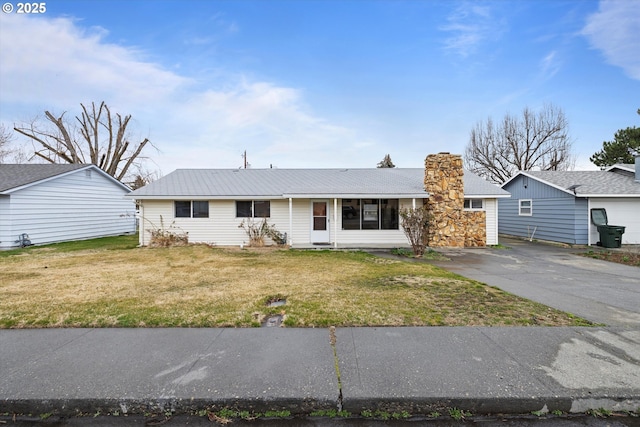 ranch-style house featuring a chimney, driveway, metal roof, and a front yard