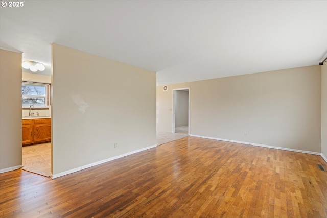 empty room featuring light wood-type flooring, baseboards, and a sink