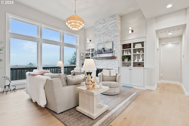 living room featuring a high ceiling, light wood finished floors, baseboards, and visible vents