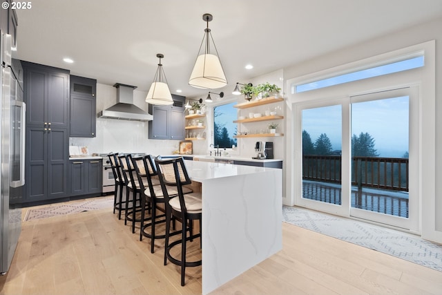 kitchen with open shelves, wall chimney exhaust hood, light countertops, light wood-type flooring, and range with gas stovetop
