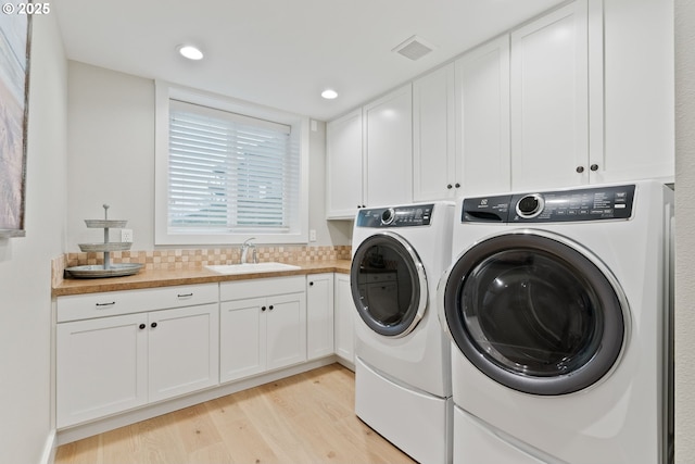 washroom featuring visible vents, a sink, light wood-type flooring, cabinet space, and washing machine and clothes dryer