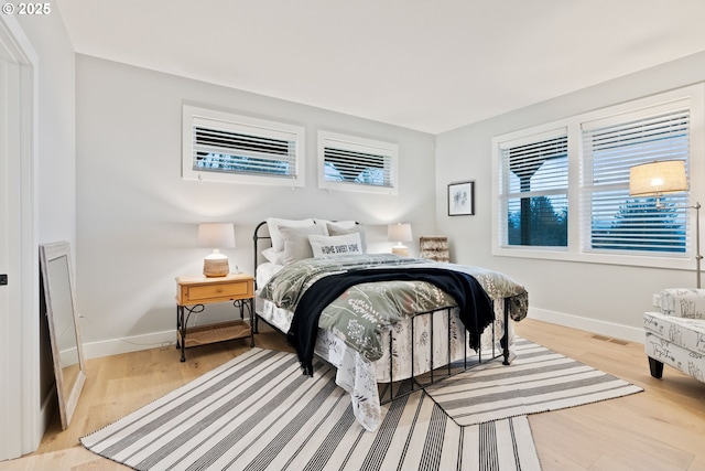 bedroom with light wood finished floors, visible vents, and baseboards