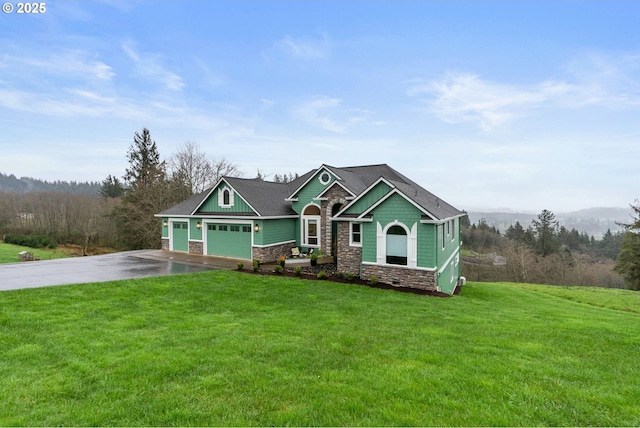 craftsman-style house featuring a front yard, an attached garage, stone siding, aphalt driveway, and a forest view