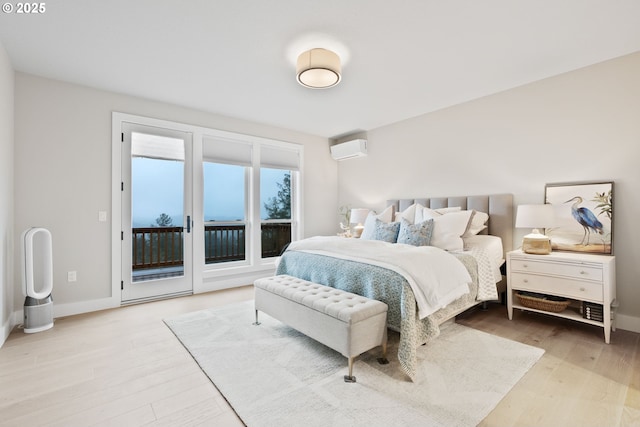 bedroom featuring access to outside, wood finished floors, a wall mounted air conditioner, and baseboards