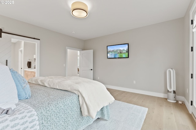bedroom featuring light wood finished floors, baseboards, connected bathroom, and a barn door