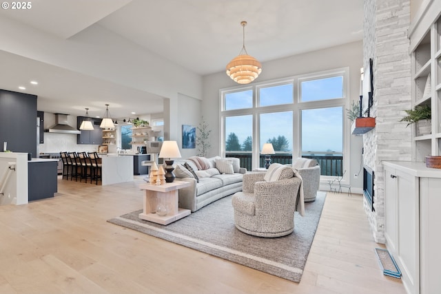 living area featuring a stone fireplace, light wood-type flooring, a towering ceiling, and recessed lighting