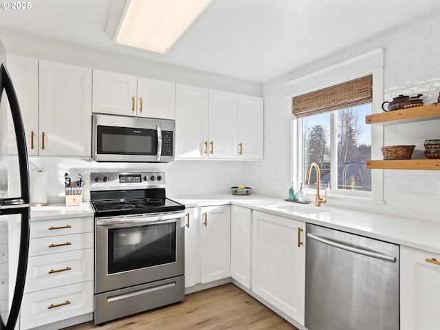 kitchen with sink, white cabinetry, tasteful backsplash, light wood-type flooring, and appliances with stainless steel finishes