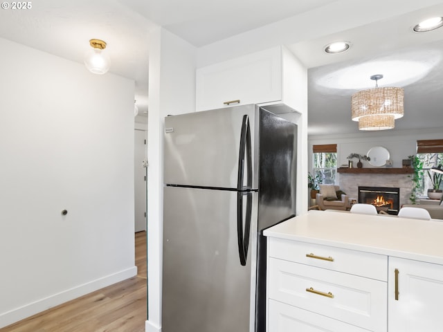 kitchen featuring white cabinetry, hanging light fixtures, stainless steel fridge, and light hardwood / wood-style flooring