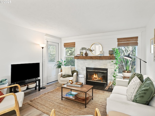 living room featuring hardwood / wood-style flooring, a healthy amount of sunlight, and a stone fireplace