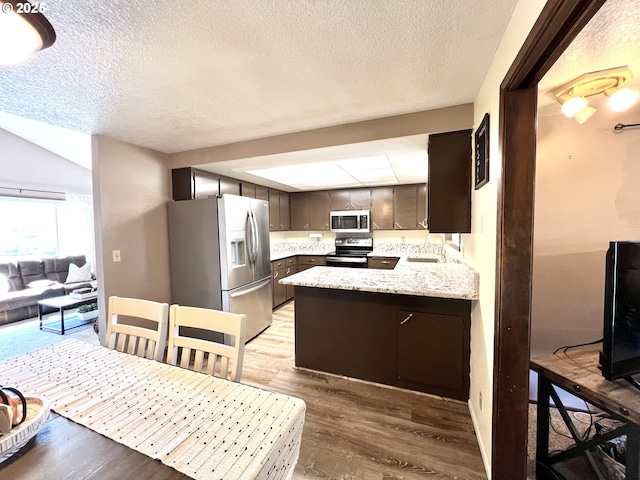 kitchen featuring light countertops, light wood-style flooring, appliances with stainless steel finishes, a peninsula, and a sink