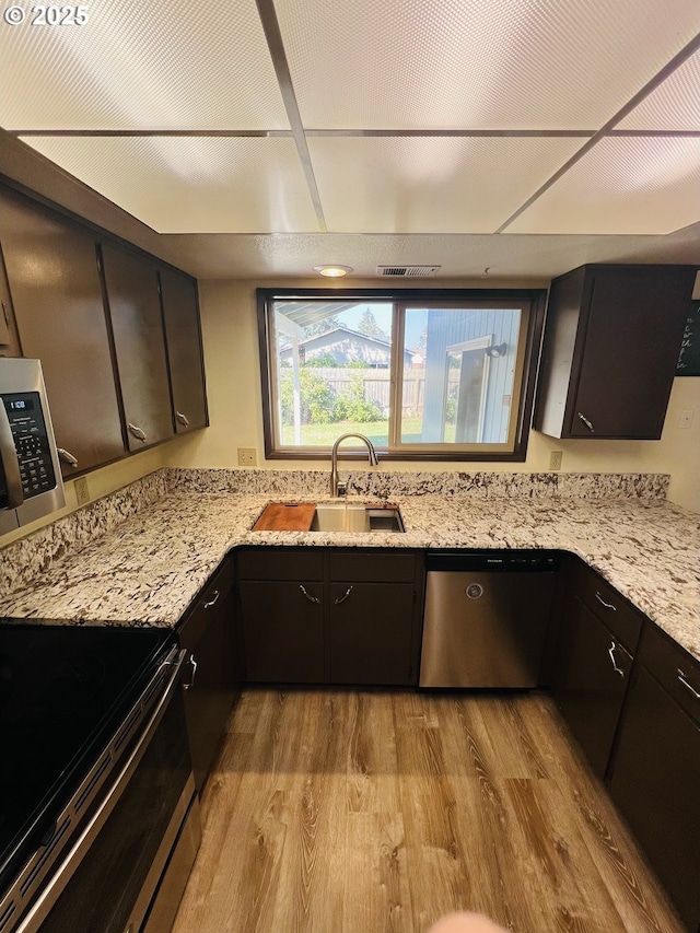 kitchen with light wood finished floors, visible vents, light stone countertops, appliances with stainless steel finishes, and a sink