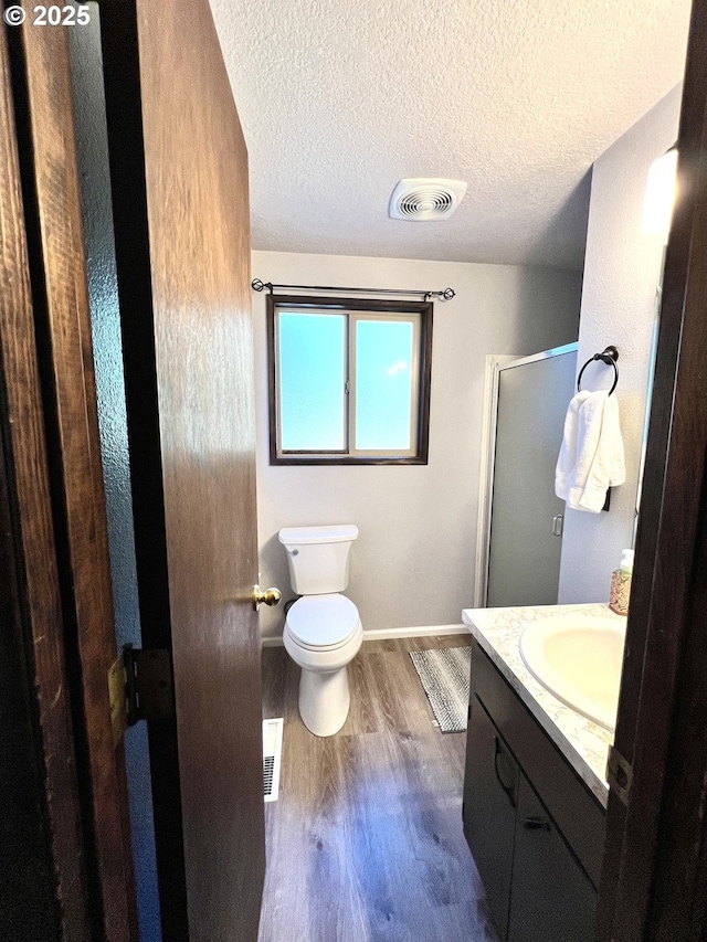 full bathroom featuring a shower stall, toilet, vanity, wood finished floors, and a textured ceiling