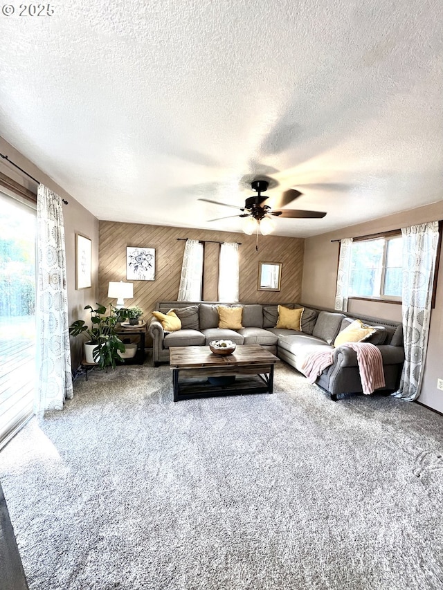 carpeted living area featuring wooden walls, a ceiling fan, and a textured ceiling