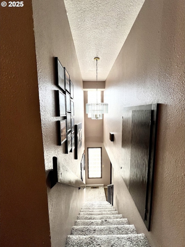 staircase with a textured ceiling, a notable chandelier, and a textured wall