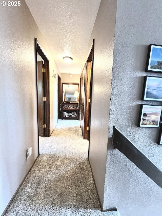 hall with a textured ceiling, a textured wall, and carpet floors