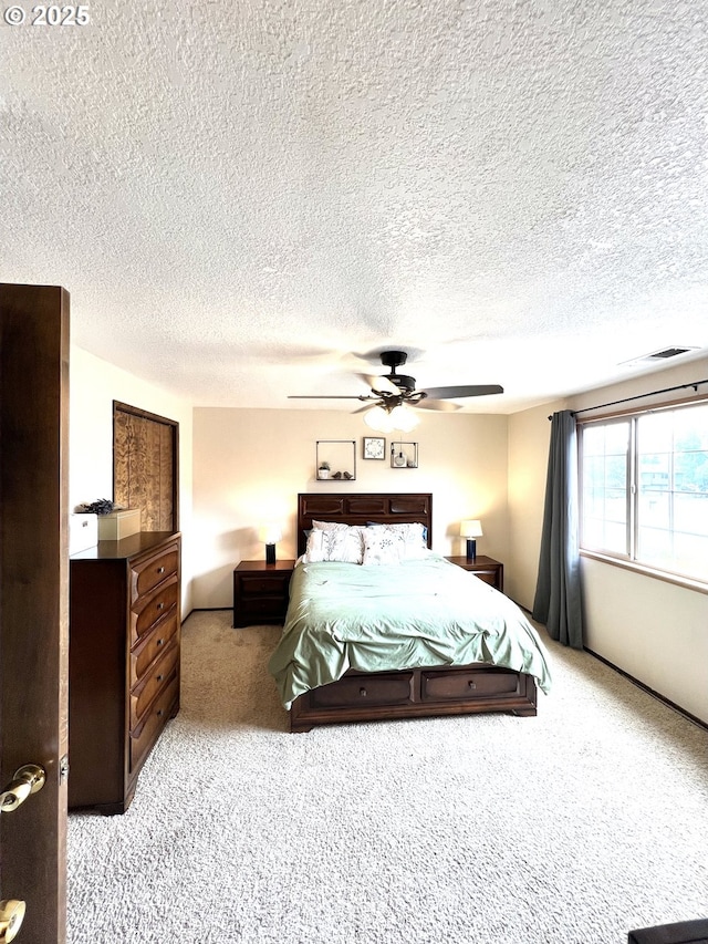 bedroom featuring a ceiling fan, light colored carpet, visible vents, and a textured ceiling